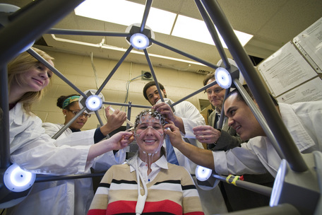 Student research subject surrounded by lab workers